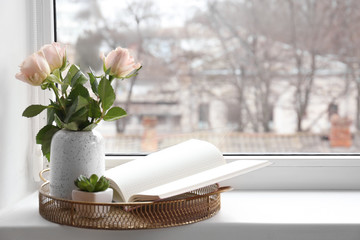 Vase with bouquet of flowers and book on window sill