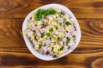 Tasty salad with sausage, green pea, canned corn, bell pepper, cucumber and mayonnaise on wooden table. Top view