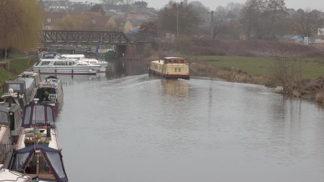 Ely, England. Big yellow narrow boat moving along the river. More boats in back ground