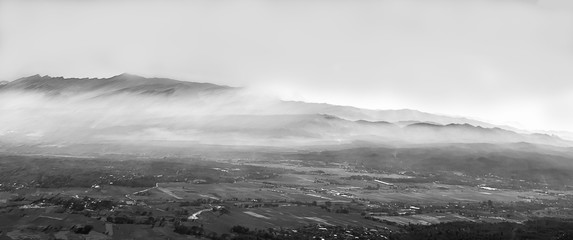 Landscape panorama black and white beautiful nature forest mountains and small town valley in fog with clear sky on sunrise.