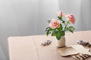 Vase with fresh rose flowers and old letters on table