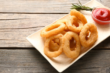Plate with tasty onion rings and sauce on wooden table