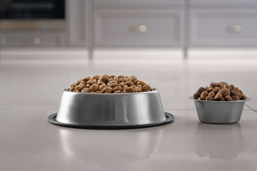 Bowls with dry pet food on floor