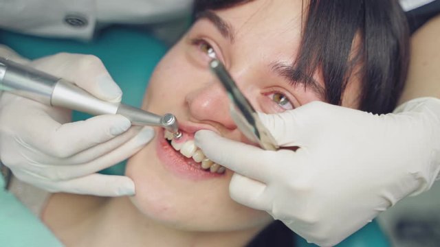 Dental hygienist polishing patient teeth in cosmetic dentistry clinic. Close up of a specialist working with patient in dentist office. Female patient moans a little during her visit at dentist.