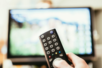 Male hand is holding TV remote control, streaming on a smart TV.