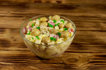 Potato salad with marinated mushrooms, sausage, onion and mayonnaise on wooden table