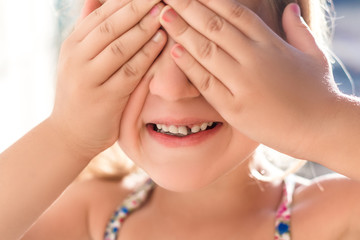 A little cute girl closes the hands of her eyes and shows a reeling baby tooth.