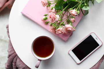 Cup of hot tea with mobile phone, flowers and book on white table