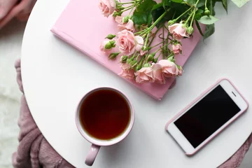 Fotobehang Cup of hot tea with mobile phone, flowers and book on white table © Pixel-Shot