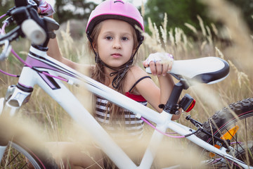 Obraz premium Little cute girl in a pink helmet near a bicycle