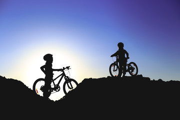 Silhouette of two little girls with bicycles at sunset