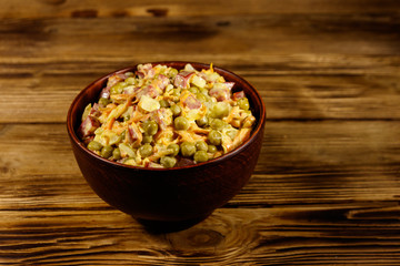Mayonnaise salad with sausage, green pea, carrot and onion on wooden table
