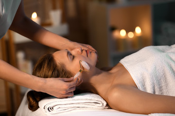 Young woman undergoing procedure of facial massage in beauty salon