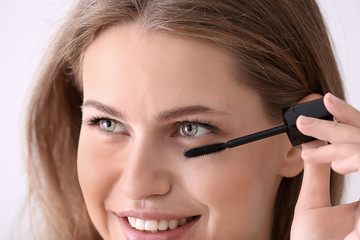 Fototapeta premium Young woman applying mascara onto eyelashes against light background, closeup