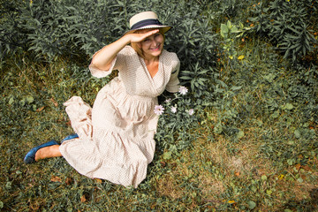 Beautiful blonde woman in hat and dress sitting on the grass