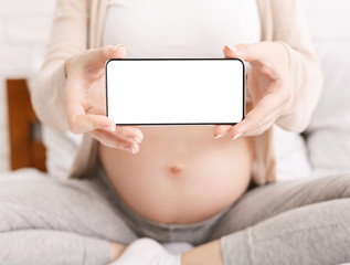 Pregnant woman holding cellphone with blank screen near her belly