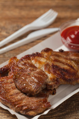 Grilled pork neck served on paper trays.