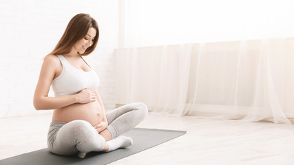 Active pregnant woman sitting on floor after doing sports