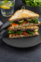 Sandwiches with cream cheese, salmon and spinach on a dark background.