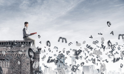Man on roof edge reading book and symbols flying around