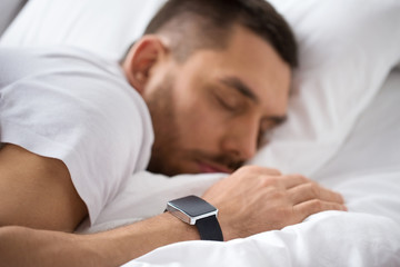 people, technology and rest concept - close up of man with smart watch sleeping in bed