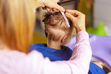 Fototapeta premium Cute little girl in hairdressing salon. Back side of a girl hair cut in barber salon