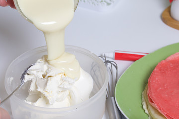 Cooking the pie with mascarpone cream. A woman prepares an impregnation of mascarpone for the cake. Adds condensed milk.