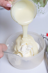 Cooking the pie with mascarpone cream. A woman prepares an impregnation of mascarpone for the cake. Adds condensed milk.