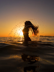 Woman in the sea at sunset flipping her hair out of the water