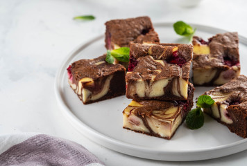 Cheesecake brownies with raspberry stacked on a white plate.