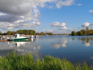 Fototapeta premium Water smooth surface of the river Kotorosl with reflecting clouds, pier with motorboats, Yaroslavl