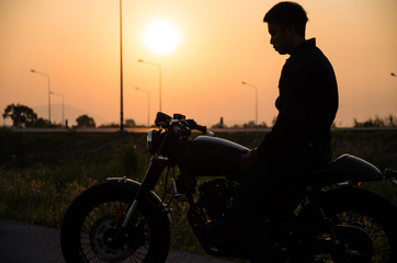 silhouette of man riding vintage motorcycle cafe racer style on sunset scene