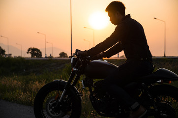 silhouette of man riding vintage motorcycle cafe racer style on sunset scene