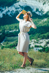 An attractive girl in a straw hat on a walk in a mountainous area enjoys a Sunny day and a good mood.