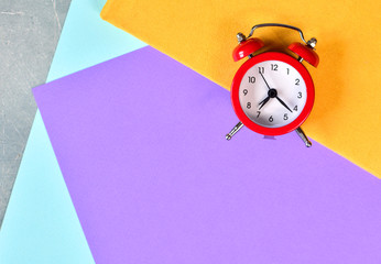Red alarm clock on a colorful paper, top view