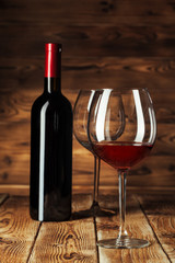Glass and bottle with delicious red wine on table against wooden background
