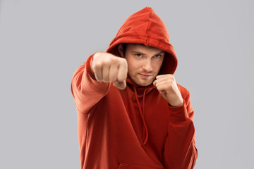 combat, aggression and people concept - young man in red hoodie fighting with fists or boxing over...
