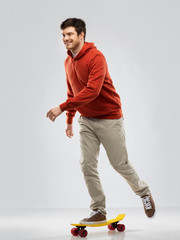leisure, sport and people concept - happy smiling young man in hoodie riding on short skateboard over grey background © Syda Productions