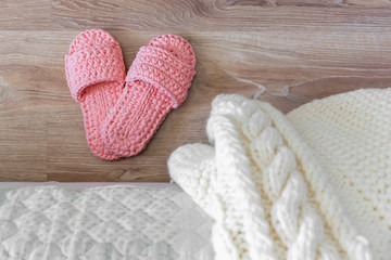 Knitted white bedspread and pink women's Slippers near the bed.