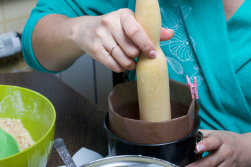 A woman seals a layer of biscuit crumbs in the form of a cake. Cooking a cake of biscuit crumbs and milk jelly. On the surface of the table are the ingredients and cooking utensils.