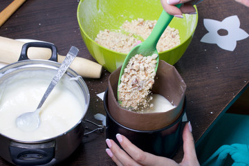 Woman adds sponge cake to cake mold. Cooking a cake of biscuit crumbs and milk jelly. On the surface of the table are the ingredients and cooking utensils.