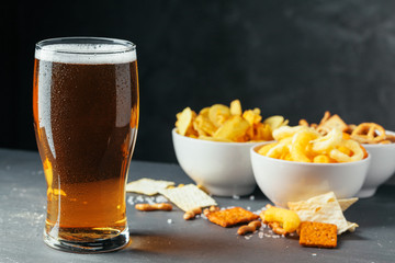 Glass of lager beer with snack bowls on dark stone background