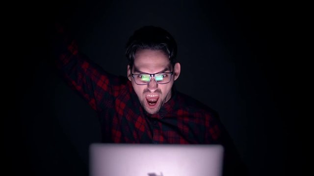 A man throws his hand up and shouts joyfully. Person looks at the monitor and is happy about winning in casino or winning his team. A man is watching football on a laptop screen.