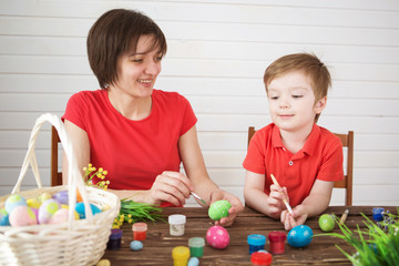 Mother and son painting Easter eggs. Happy family Mom and children son paint easter eggs with colors. Preparation for holiday.