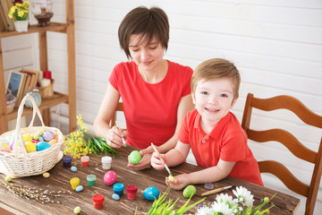 Easter preparations. Happy young mother spending time with her joyful son. Happy family Mom and children son paint easter eggs with colors. Preparation for holiday.