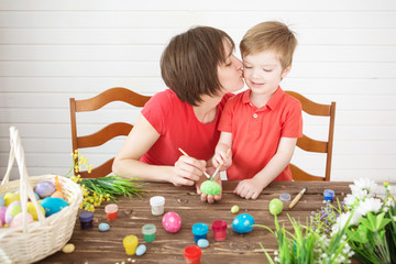 Smiling happy mother and child painting easter eggs. Happy family Mom and children son paint easter eggs with colors. Preparation for holiday.