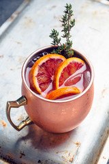 Red oranges cocktail in copper mug (variation of Moscow mule) on the wooden background. Selective focus. Shallow depth of field.
