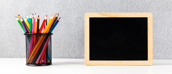 colorful pencils and chalkboard on a desk with gray background