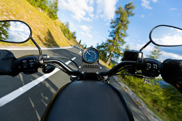 Motorcycle driver riding in Alpine highway, handlebars view, Austria, central Europe.
