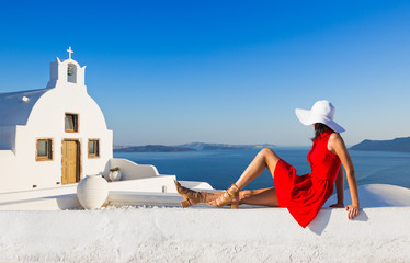 Santorini travel tourist brunette woman in red dress visiting famous white Oia village. Greece, Europe.